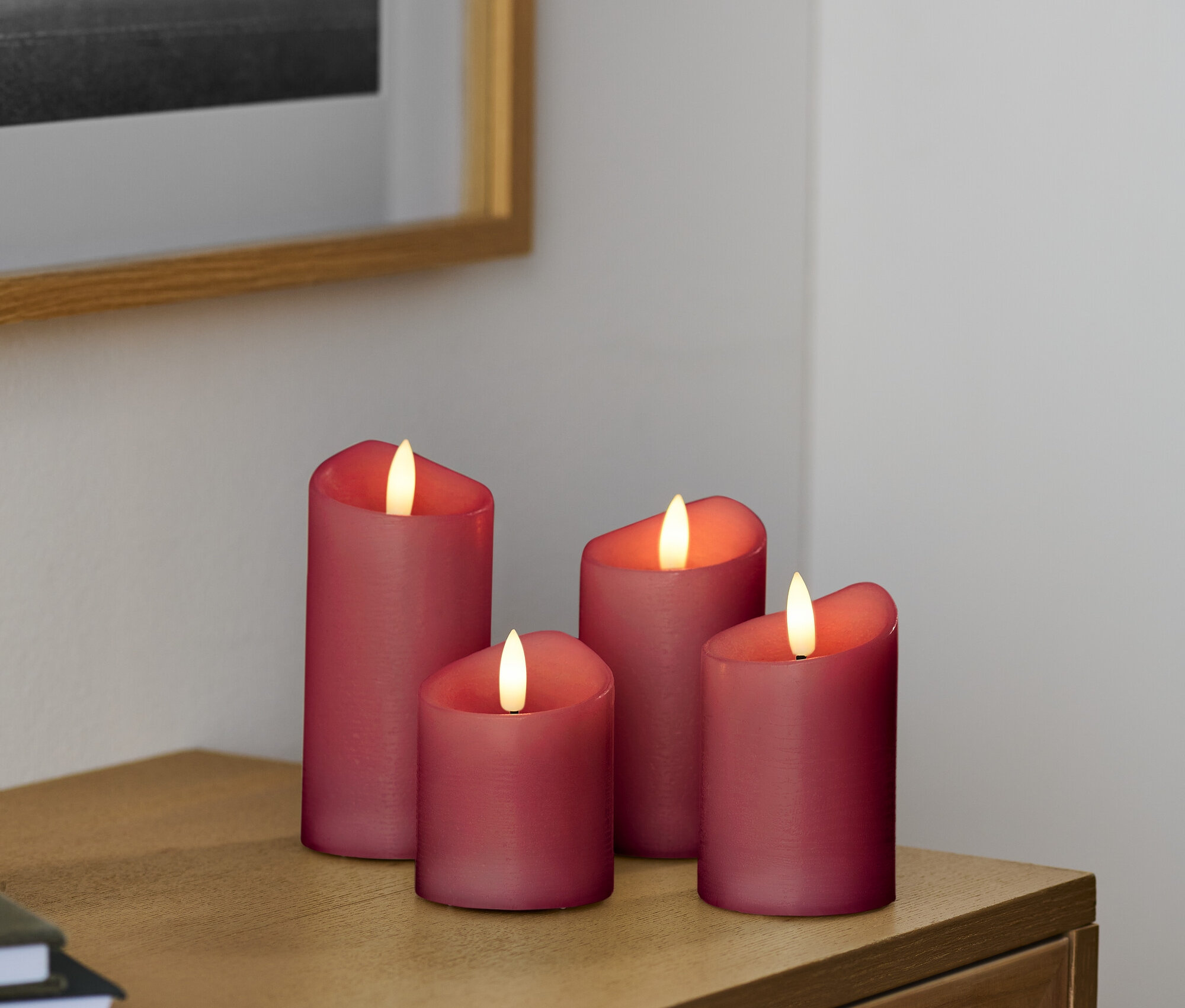 Quatre bougies LED rouges sur une commode en bois.