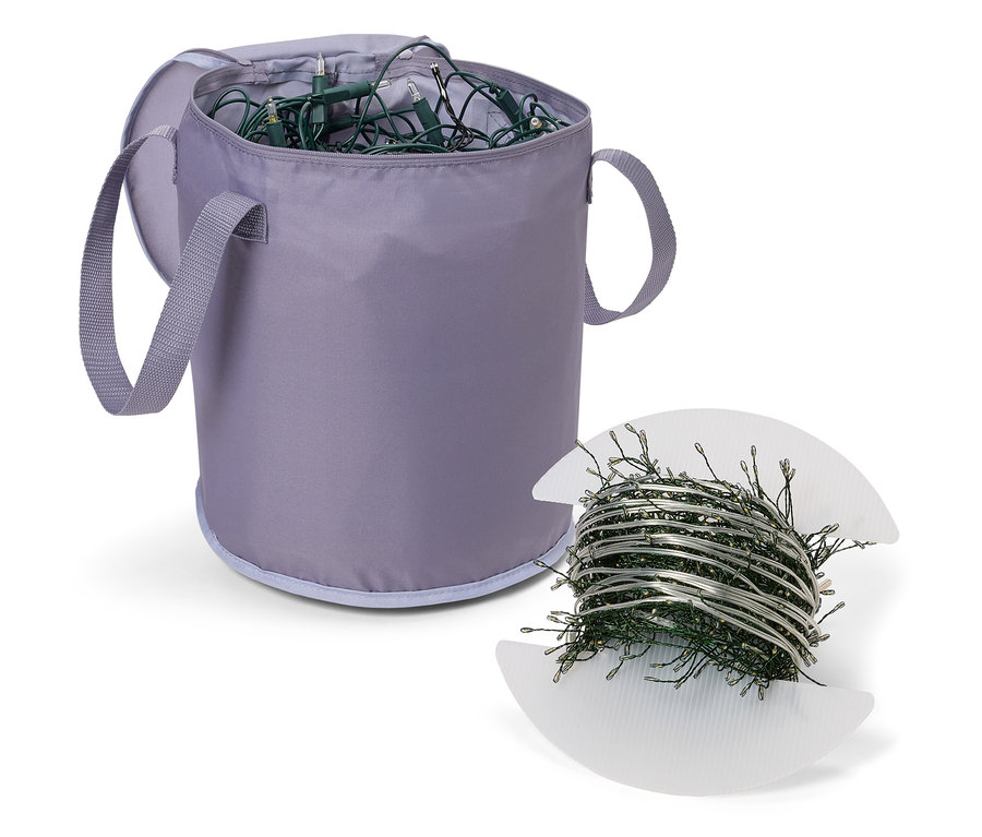 Un panier de rangement en tissu gris avec des guirlandes lumineuses de Noël à l'intérieur et une bobine de guirlandes lumineuses de Noël sur une bobine en plastique blanc à côté du panier.