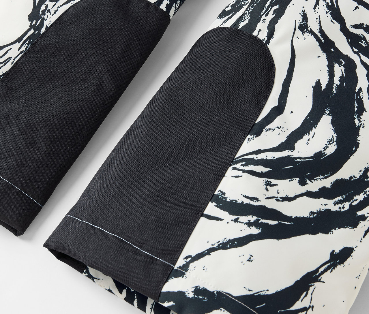Détail d'un pantalon noir et blanc avec un motif abstrait et des patchs noirs aux genoux.