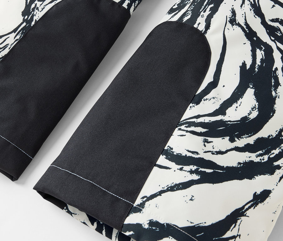 Détail d'un pantalon noir et blanc avec un motif abstrait et des patchs noirs aux genoux.
