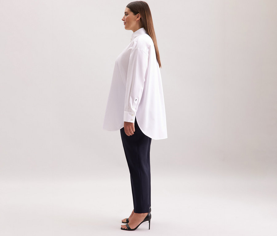Femme portant une blouse-chemise blanche grande taille Seidensticker, un pantalon foncé et des talons hauts noirs.