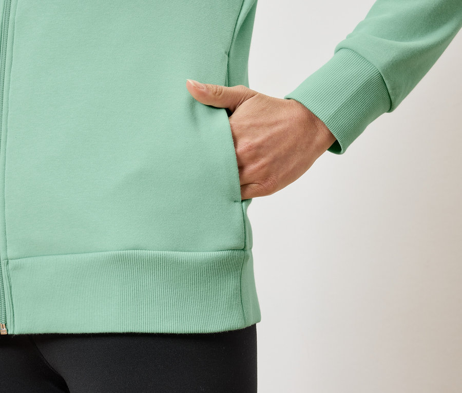 Détail d'un sweat-shirt zippé vert clair pour femme avec une main dans la poche.