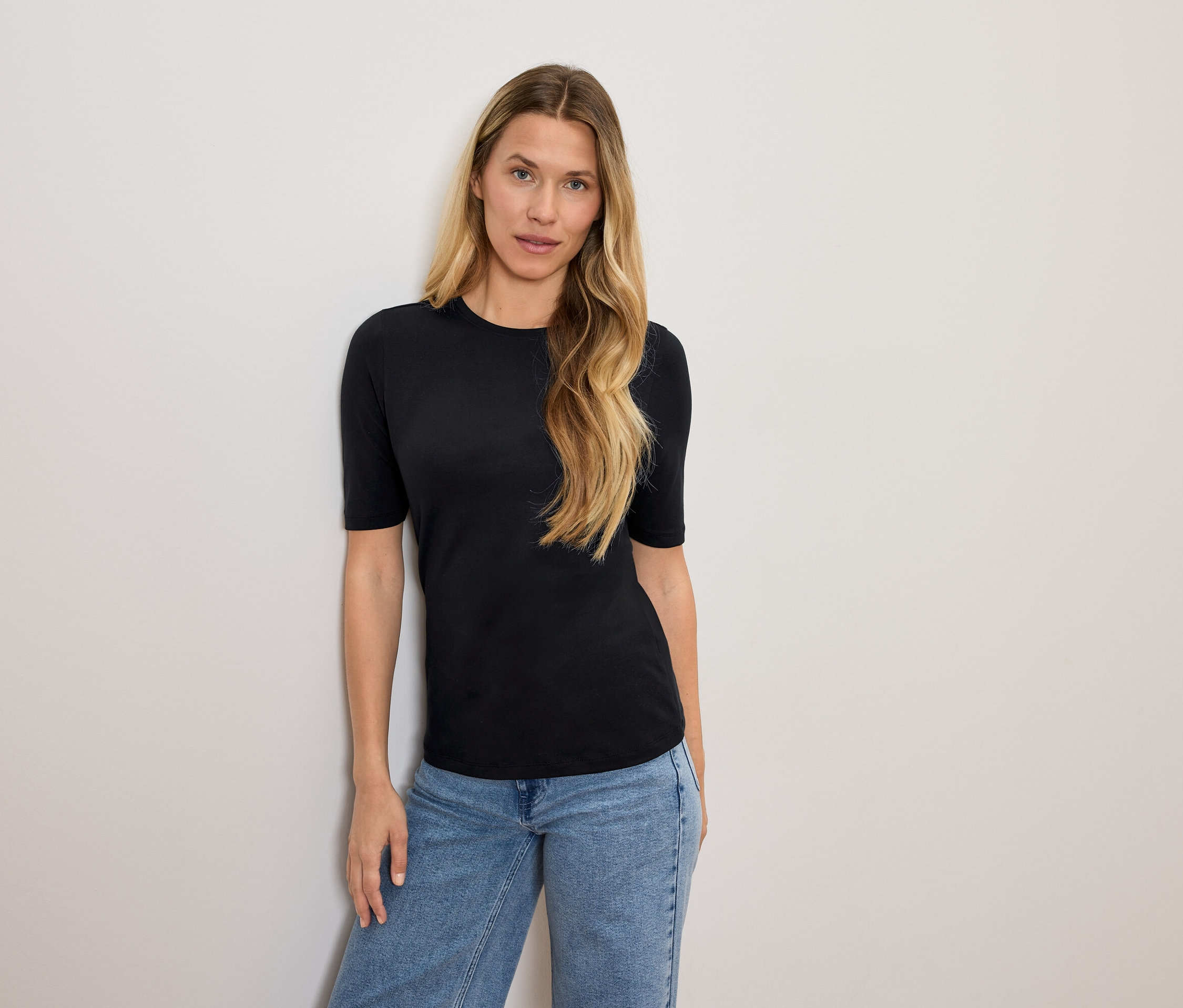 Femme blonde posant en t-shirt noir et jean bleu.