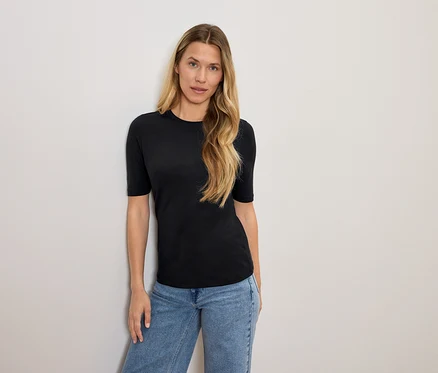 Femme blonde posant en t-shirt noir et jean bleu.
