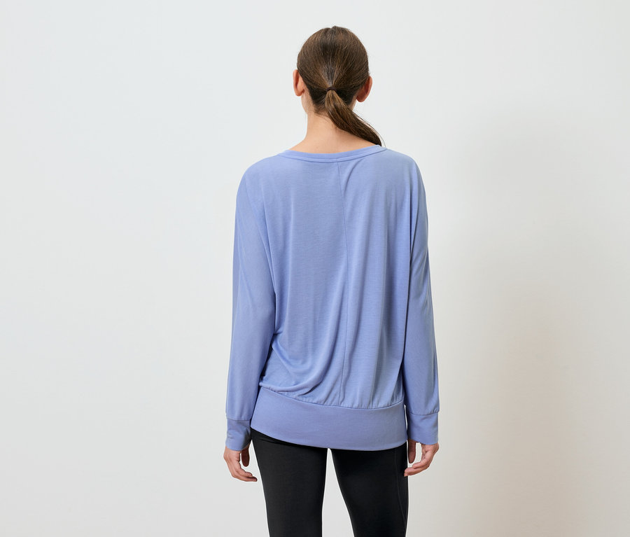 Une femme, vue de dos, porte un haut bleu à manches longues et un pantalon noir.