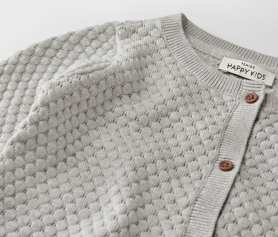 Gros plan sur une veste en maille grise pour bébé.