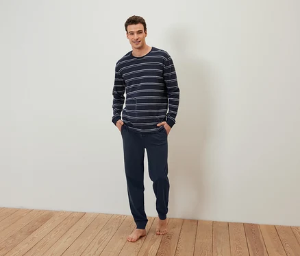 Un homme pieds nus se tient debout, les mains dans les poches d'un pyjama bleu marine rayé.