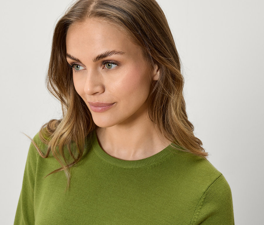 Portrait d'une femme aux cheveux bruns ondulés portant un pull vert, regardant sur le côté.