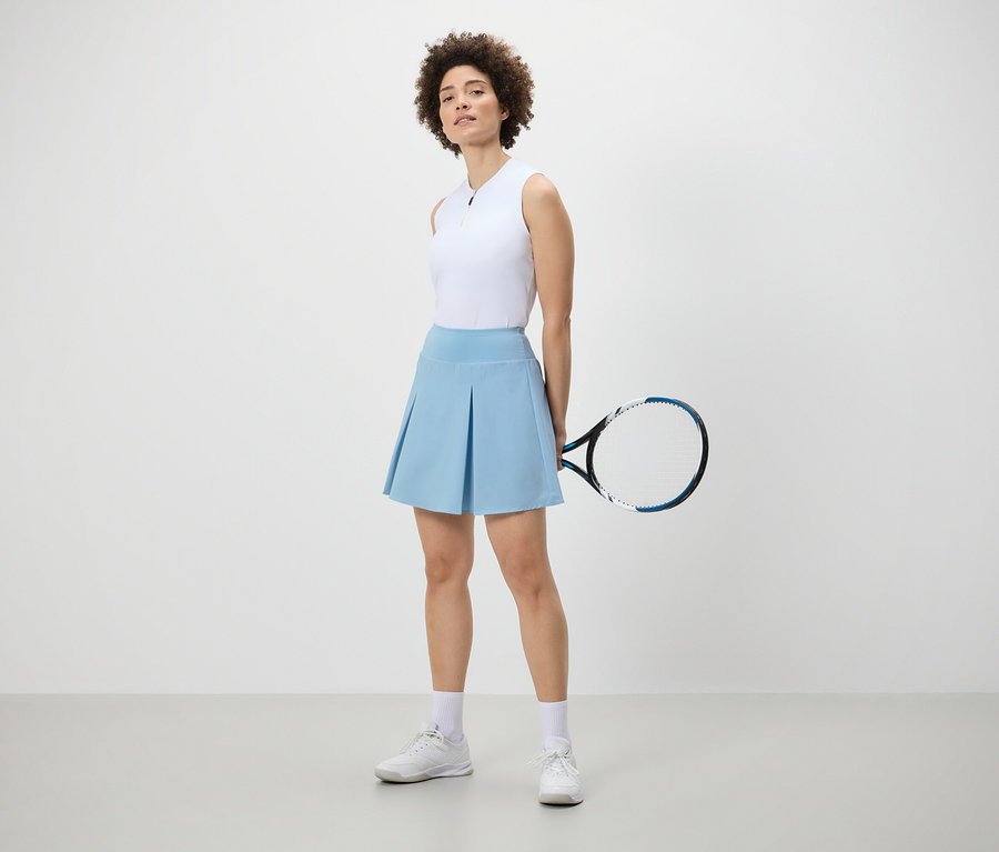 Femme posant avec une jupe de sport bleu clair et une raquette de tennis.