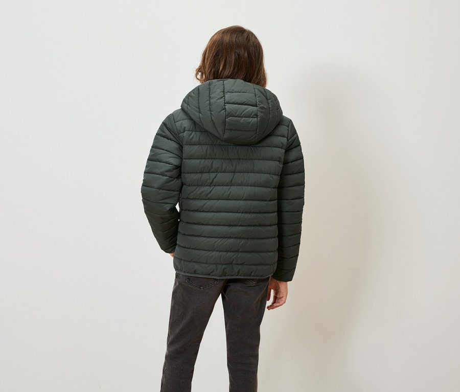 De dos, une personne aux cheveux bruns portant une veste matelassée verte à capuche et un jean gris.