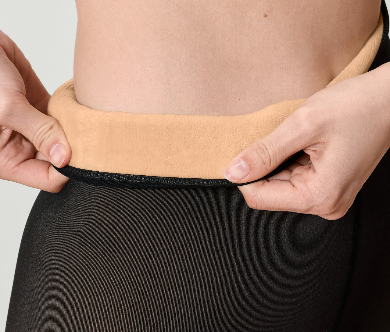 Gros plan d'une femme remontant la taille de collants noirs avec une doublure en polaire beige.