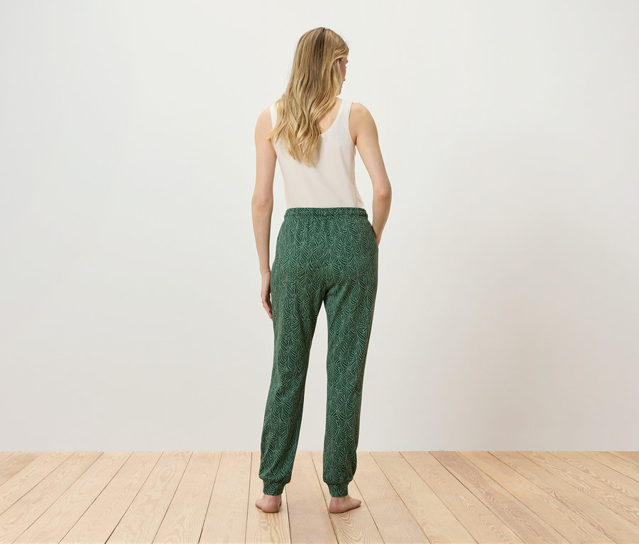 Une femme en débardeur et pantalon vert à motifs, dos à la caméra.
