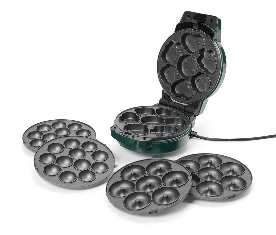 Un appareil à donuts vert est ouvert, présentant différents moules dont un cœur, une étoile et un smiley. Quatre plaques à donuts grises accompagnent l'appareil.