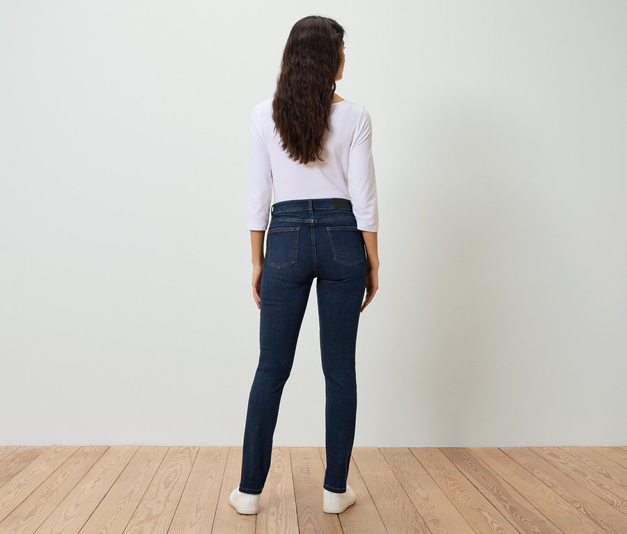 Une femme, vue de dos, porte un jean bleu et une chemise blanche.