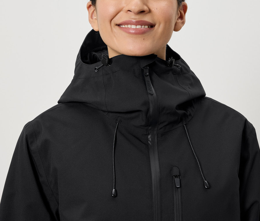 Une femme souriante porte une veste noire à capuche.