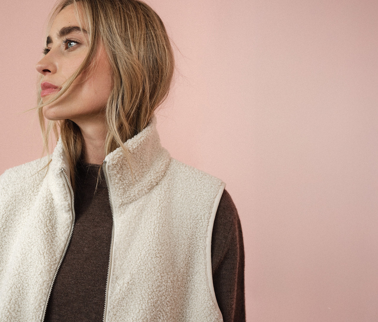 Femme portant une veste en teddy Street One sur un pull marron, regardant vers la gauche devant un fond rose.