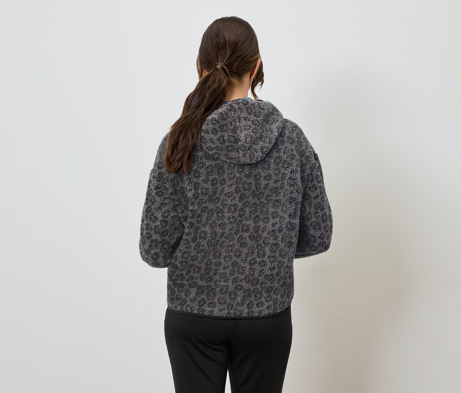 Une femme, dos à la caméra, porte un sweat à capuche gris à motif animal et un pantalon noir.