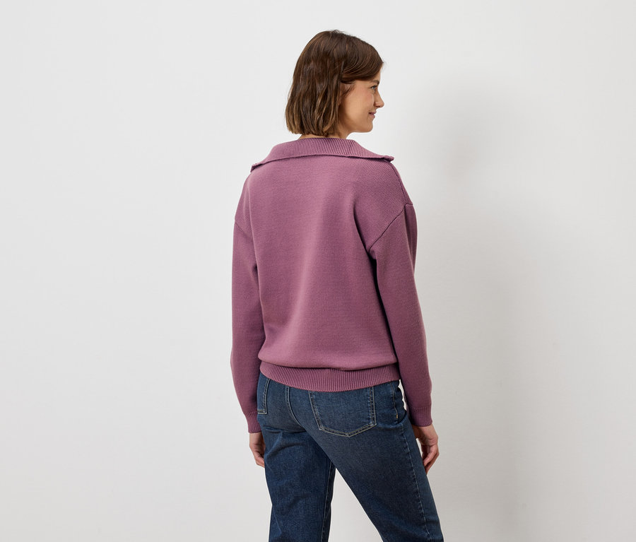 Une femme, dos à la caméra, porte un sweat-shirt violet et un jean.
