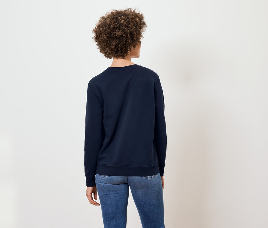 Une femme aux cheveux bouclés, vue de dos, porte un sweat-shirt bleu marine et un jean.