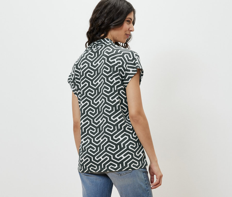 Une femme de profil porte une blouse verte avec encolure en V et un jean.