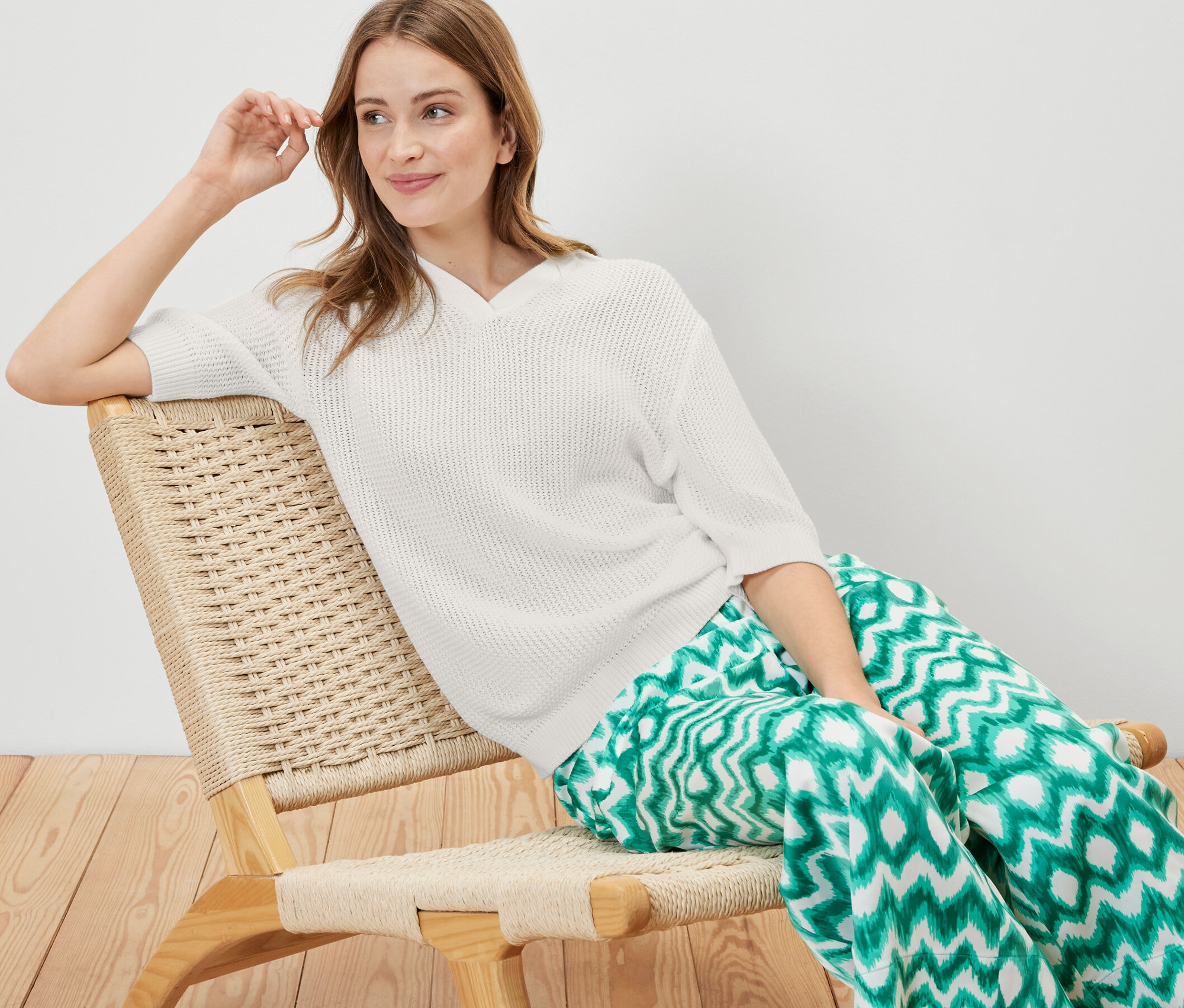Femme assise dans un fauteuil portant un pull d’été en maille.