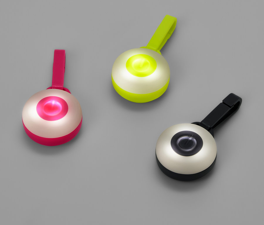 Trois lumières rondes avec des clips en rose, vert et noir sur un fond gris.