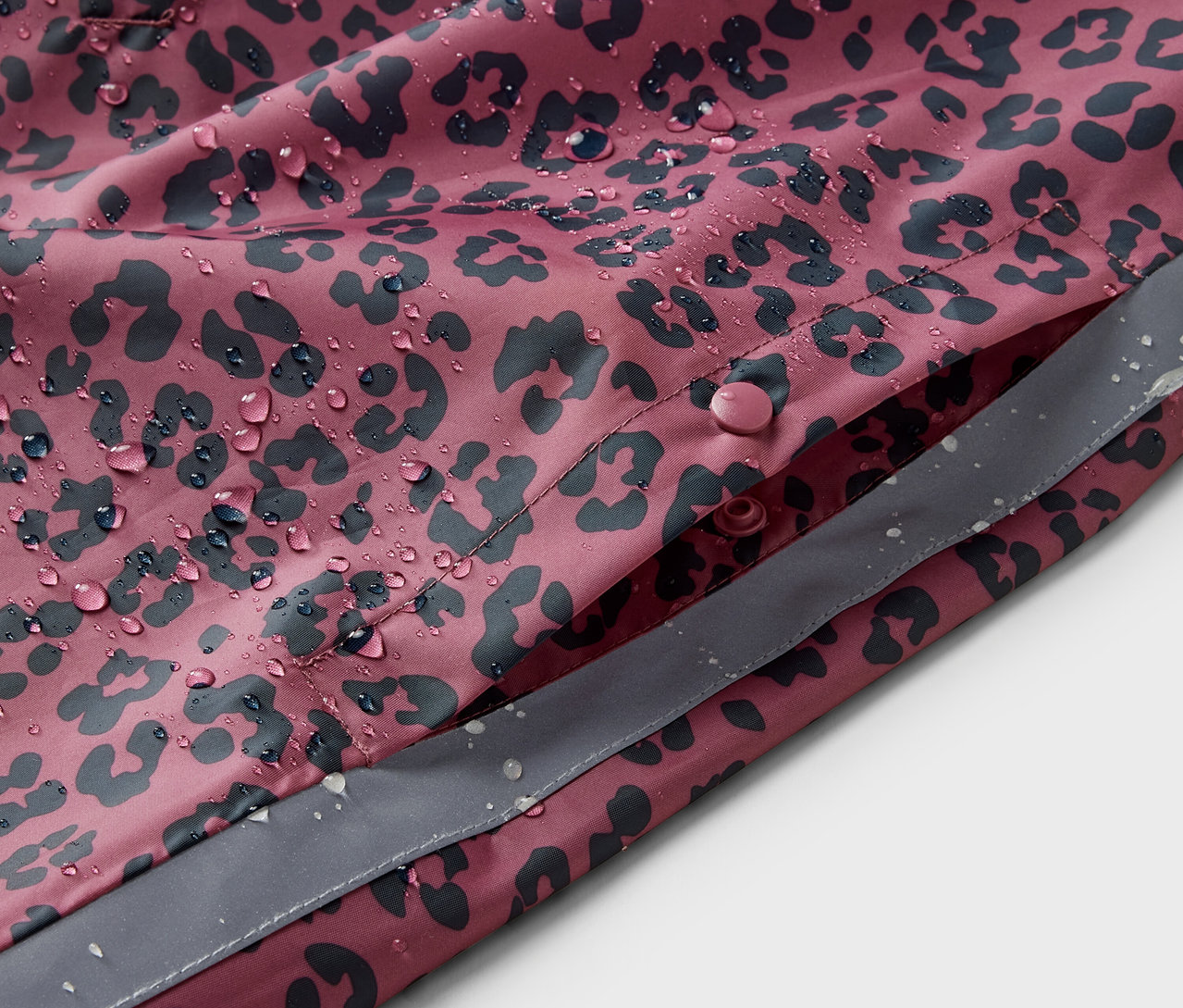 Gros plan sur un poncho de pluie rose pour enfant avec un imprimé intégral et des gouttes d'eau.