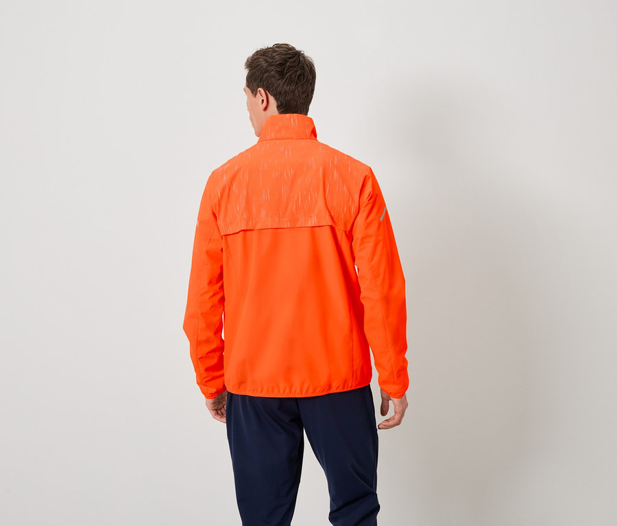 Un homme vu de dos porte une veste orange et un pantalon bleu marine.
