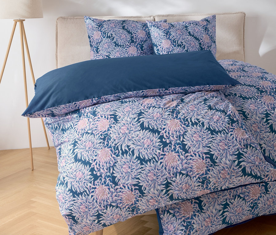 Gros plan d'un lit avec des draps à motifs floraux et un oreiller bleu.