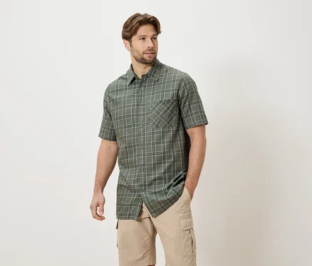 Homme portant une chemise à carreaux à manches courtes et un short cargo beige, une main dans la poche.