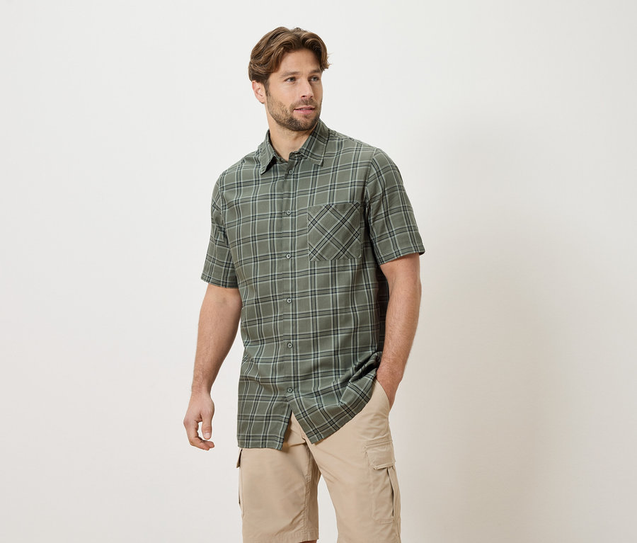 Homme portant une chemise à carreaux à manches courtes et un short cargo beige, une main dans la poche.