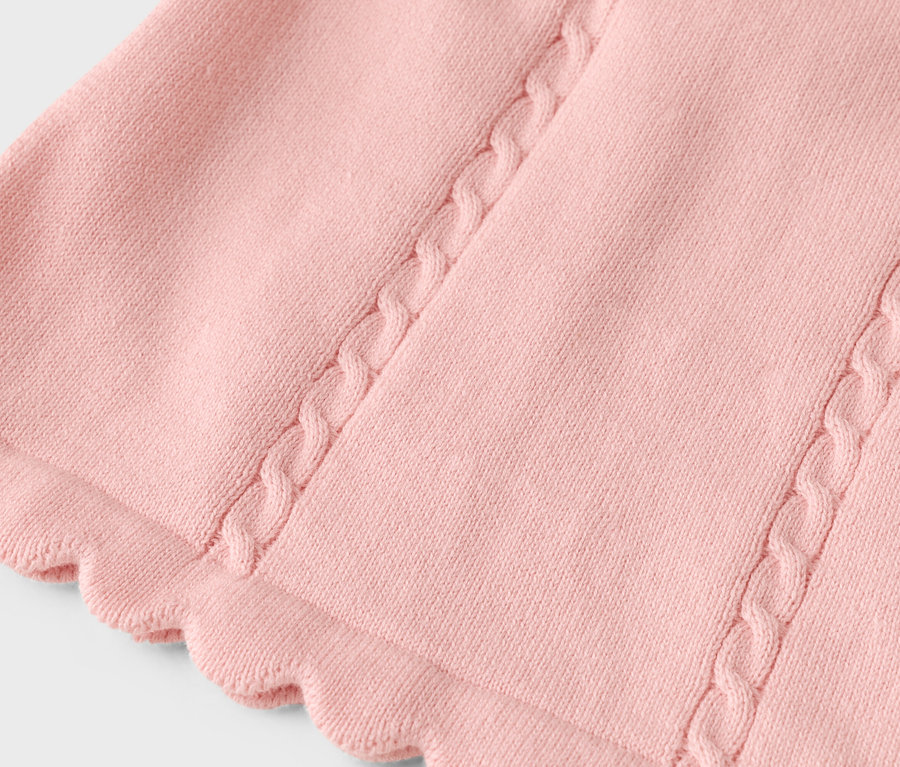 Gros plan d'un tricot rose avec des détails de torsades et un ourlet ondulé.