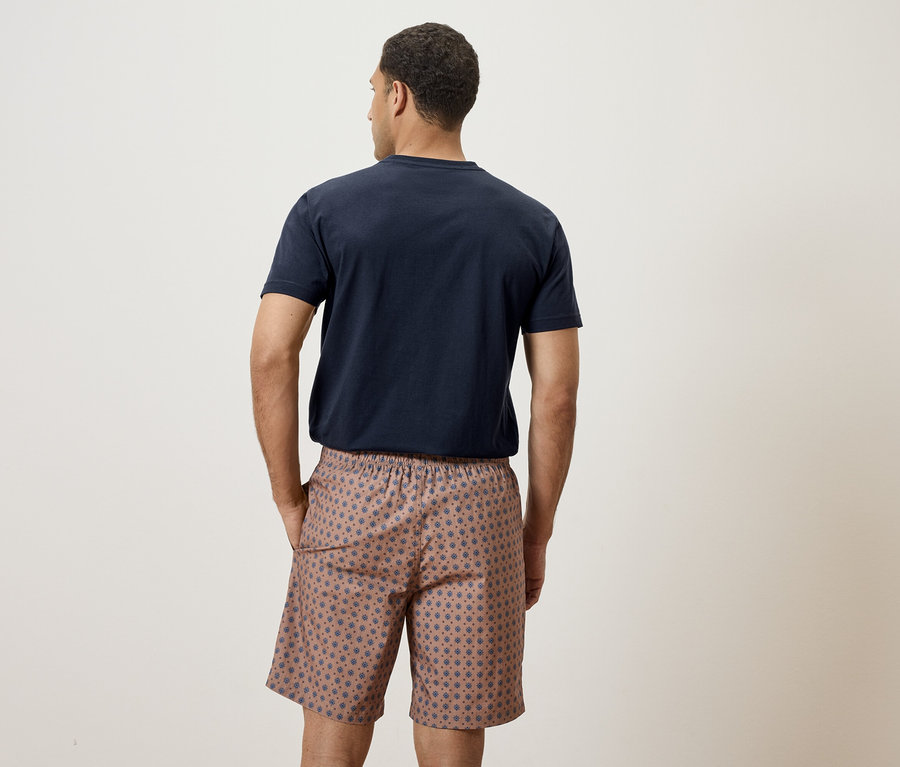 Homme vu de dos portant un t-shirt bleu marine et un short à motifs.
