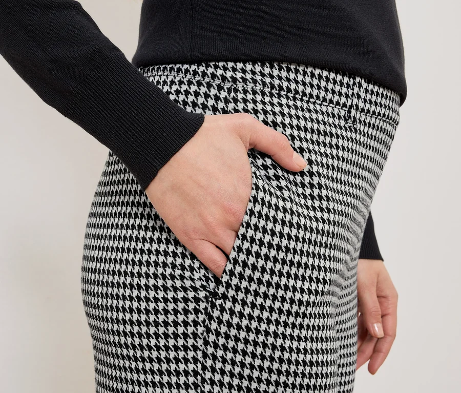 Femme avec la main dans la poche d'un pantalon à carreaux noir et blanc et un pull noir.