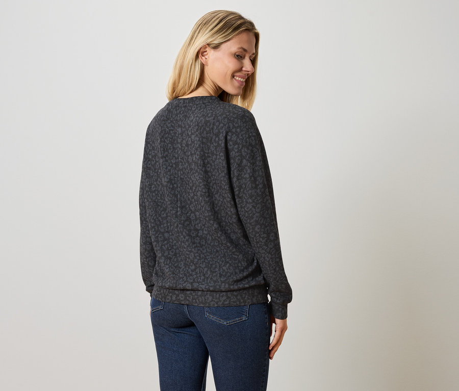 Femme portant un pull gris foncé à motif léopard et un jean bleu.