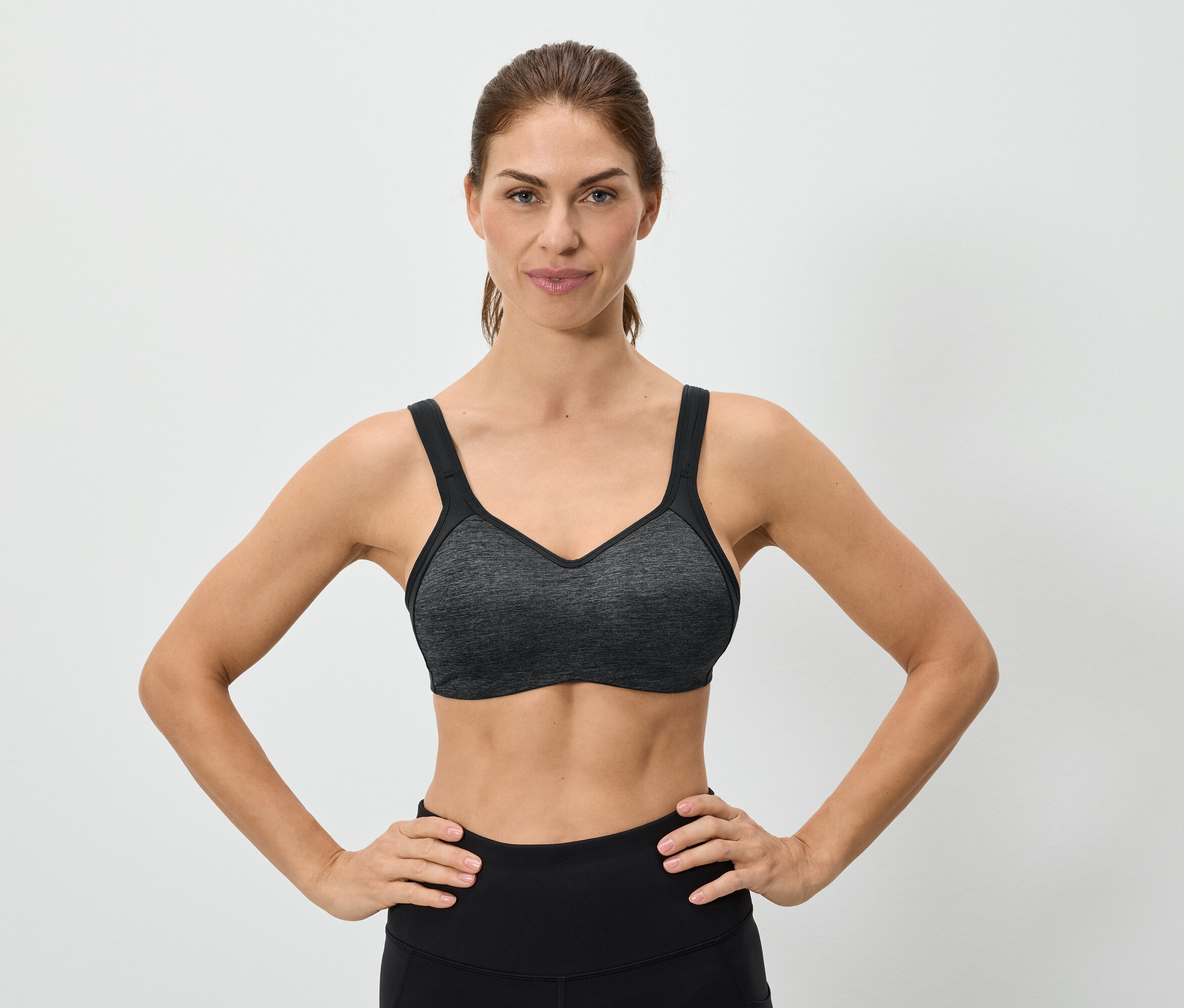 Femme les mains sur les hanches portant un soutien-gorge de sport gris.