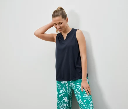 Une femme aux cheveux blonds porte un haut foncé et un pantalon vert avec des motifs blancs.