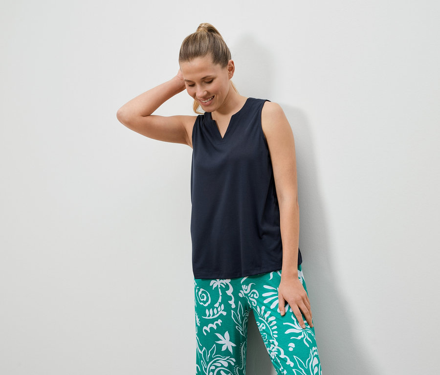 Une femme aux cheveux blonds porte un haut foncé et un pantalon vert avec des motifs blancs.