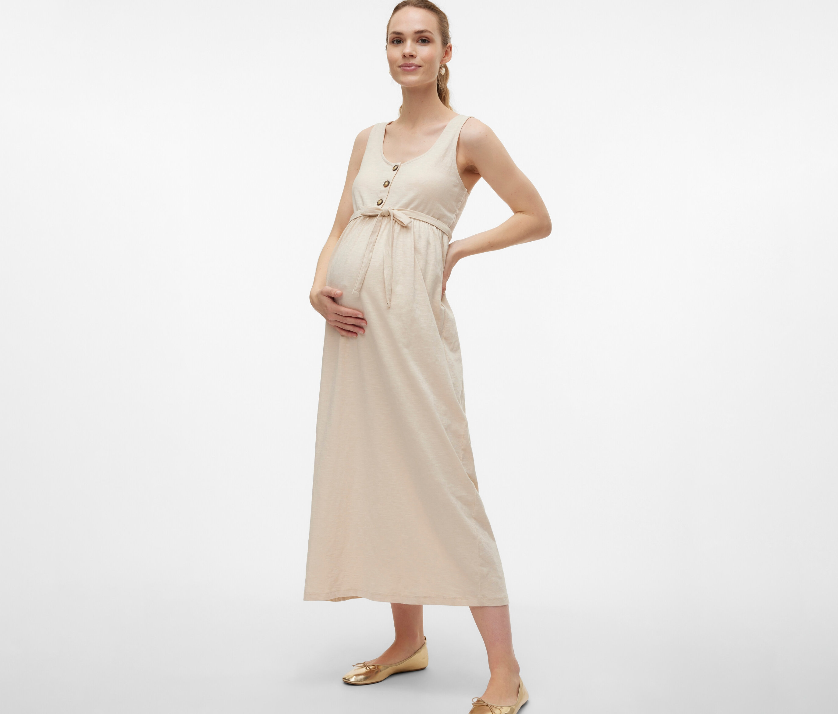 Femme enceinte portant une robe de grossesse MAMALICIOUS «
MLEVI LIA » avec ceinture et boutons, posant les mains sur le ventre et la hanche.