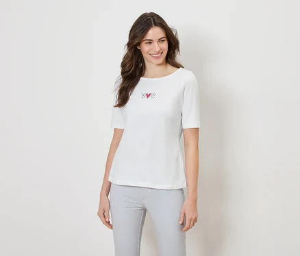 Une femme porte un t-shirt blanc avec trois cœurs et un pantalon rayé.