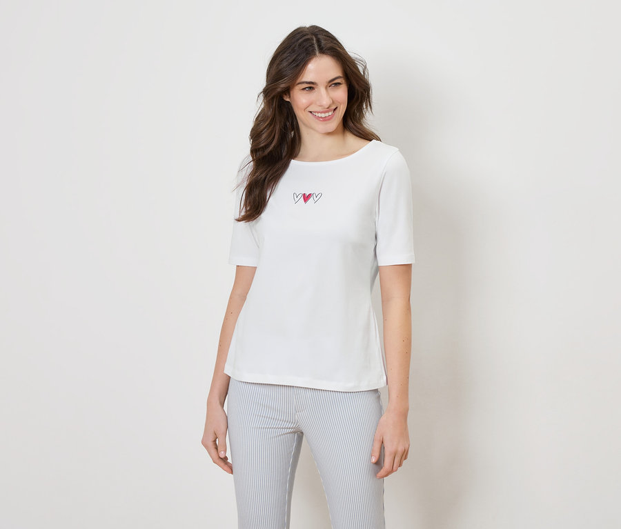 Une femme porte un t-shirt blanc avec trois cœurs et un pantalon rayé.