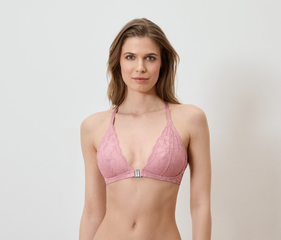 Une femme porte un soutien-gorge en dentelle rose devant un fond blanc.
