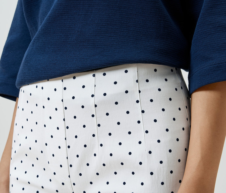 Gros plan d'une femme portant un haut bleu et un pantalon blanc à pois noirs.