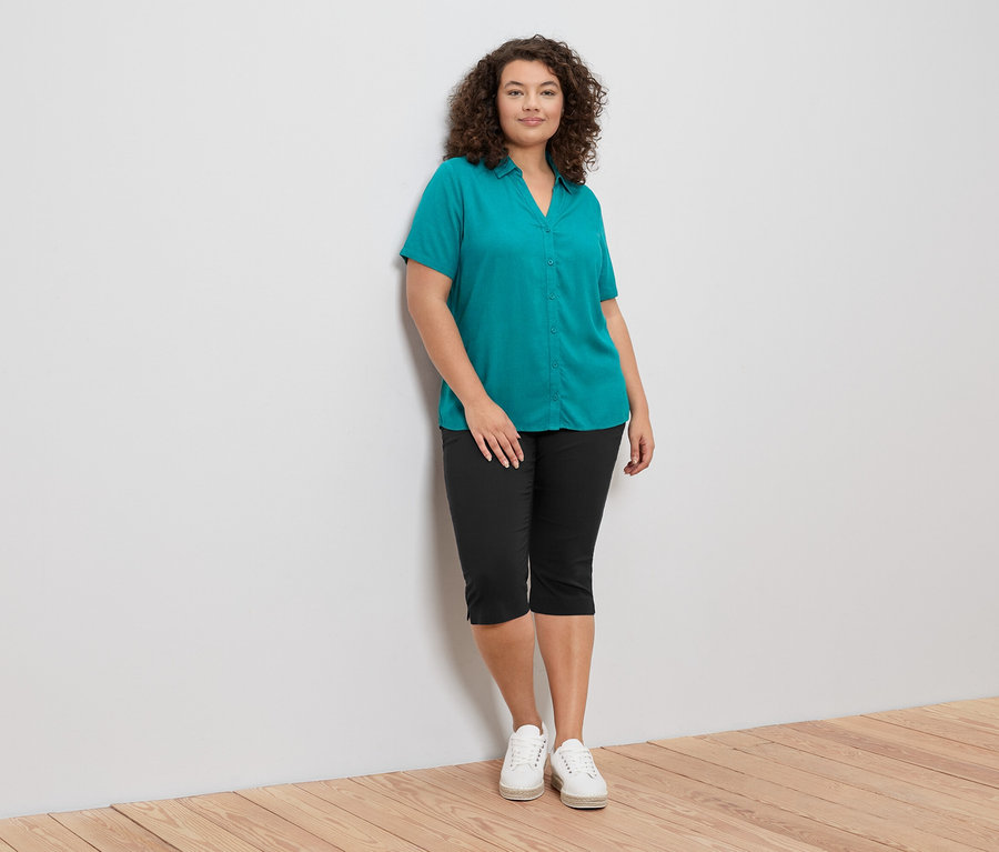 Femme portant un chemisier vert et un pantacourt noir 3/4-Bengalin-Hose. Elle porte des chaussures blanches.