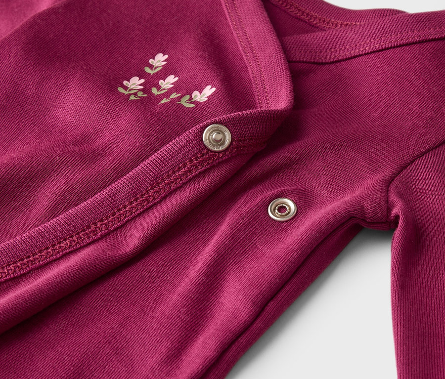 Gros plan d'une combinaison de bébé bordeaux à manches longues, avec boutons-pression et broderie florale.