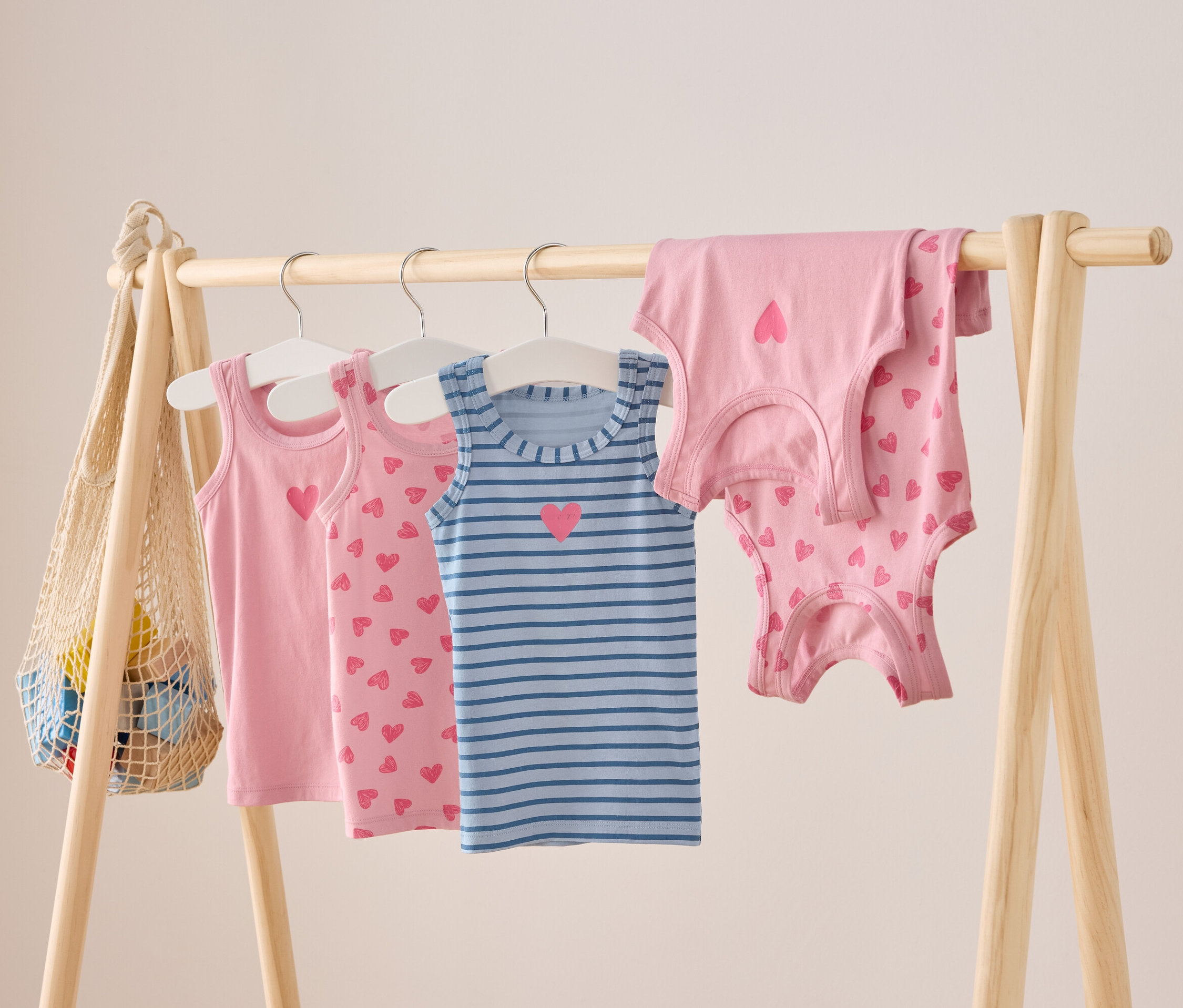 Des débardeurs pour enfants roses et bleus rayés avec des motifs de cœur sont suspendus à une barre en bois.