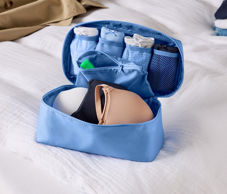 Organisateur de bagage bleu clair ouvert avec soutiens-gorge et sous-vêtements sur un drap blanc.