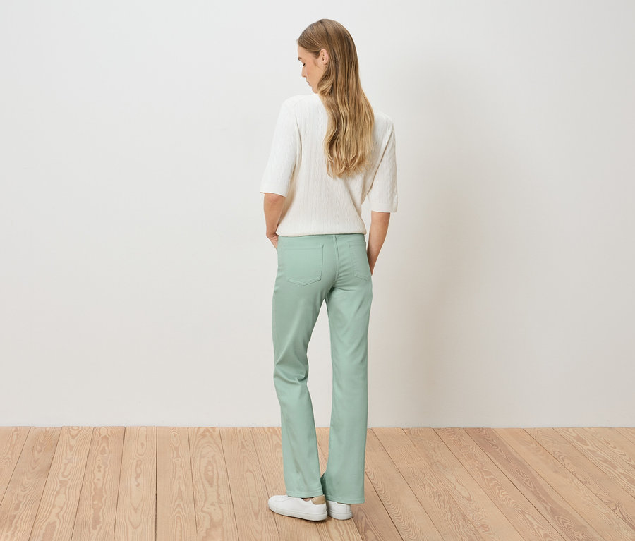 Vue arrière d'une femme blonde portant un pull blanc et un pantalon vert clair.