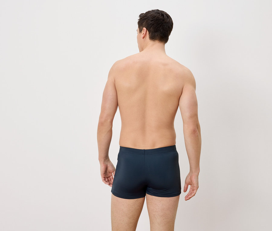 Un homme vu de dos portant un short de bain bleu.
