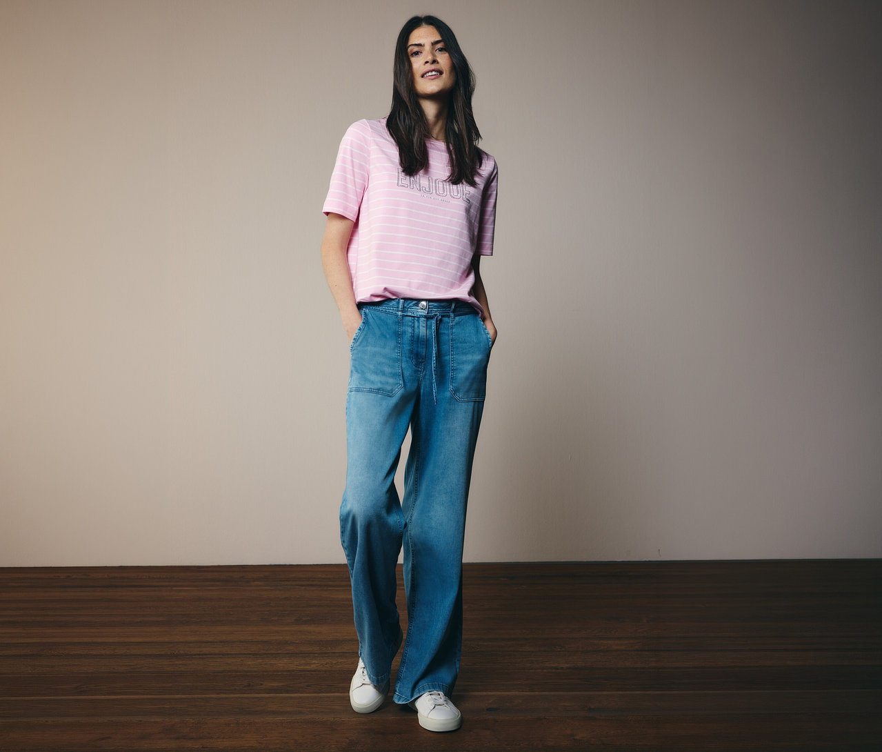 Femme portant un T-shirt CECIL à rayures roses et un jean large avec des baskets blanches, posant les mains dans les poches.